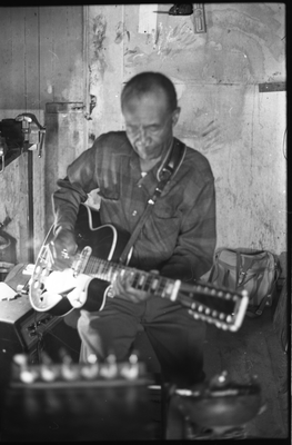 Blues musician Jesse Fuller playing guitar in his basement