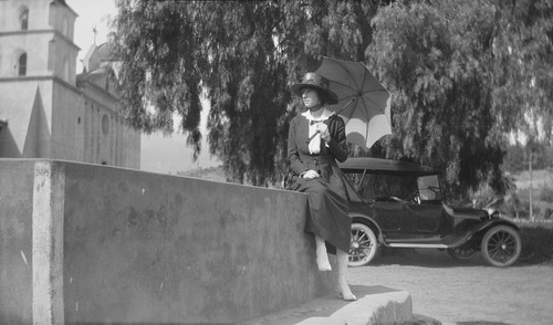 [Margaret O'Shaughnessy?] seated on a wall near a mission