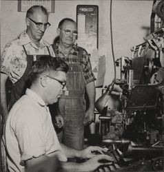 Ed Mannion at a linotype machine with 2 men watching, Petaluma, California, 1960