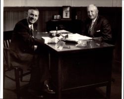 Nathan C. Thompson and Max Poehlmann seated at a desk, Petaluma, California, about 1952