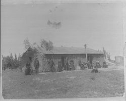 Unidentified adobe house with many people in front