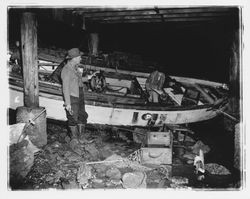 Fishermen inspecting their damaged boat washed ashore under a dock, Bodega Bay, California, January 1959