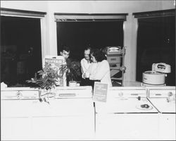 Three people looking at a washing machine during The Washing Machine Man open house, Santa Rosa, California, 1965