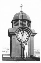 Man standing on the Masonic building roof in front of the town clock, Petaluma, California, January 1961