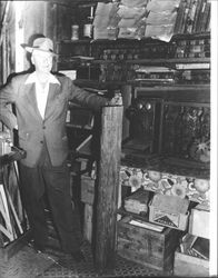 Unidentified man standing in front of shelves of artifacts, Petaluma, California, about 1970