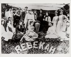 Women of the Rebekah Lodge in costume, posing atop redwood garlands, surrounding a Greek urn, photographed between 1915 and1925