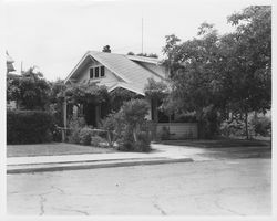 Unidentified two-story Craftsman-style home with a wisteria-covered arbor over the driveway and located on an urban street, 1960s or 1970s