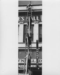 Fireman and others on a ladder leaned up against the Gossage Building at 9 Main Street, Petaluma, California, trying to put out a fire at Rex Hardware and Schindler's Bakery, 1942