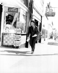 Postman Hubert Smith passing Davis Poultry Clinic and Sam's Rendezvous with Newsstand