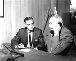 Charles De Meo talking on the telephone sitting next to William Romadka at the grand opening of Summit Savings, Sebastopol, California, September 30, 1967