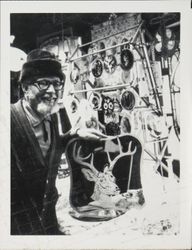 Stained glass artist in front of a crafts fair display of his work, holding a decorative window hanger featuring a buck with a large rack of antlers, 1970s