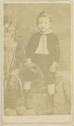 Portrait of an unidentified boy with a hat resting on his leg