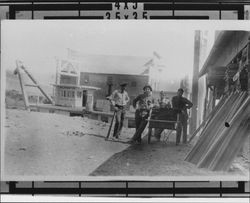 Men gathered around a cart full of lumber while the Wilmington Dredger works in the background, Petaluma, California, 1914