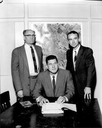 Three men in front of an aerial photograph of Petaluma