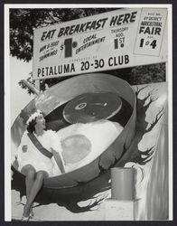 Sonja Klemenock sits in large frying pan to advertise the Petaluma 20-30 Club breakfast at 4th District Agricultural Fair, Petaluma, California, 1957