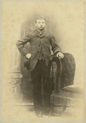 Portrait of William H. Hudson holding a hat and standing next to a chair