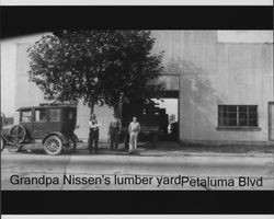 Jacob Nissen standing in front of his lumber yard on Petaluma Boulevard (Petaluma, California), with his son Russell and an unidentified man., about 1932