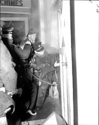 Petaluma Fire Department firefighters breaking the lock on a door at an unidentified commercial structure fire, 1950s