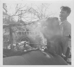 Unidentified man carrying a smoking mattress to a pile of other burned furnishings during a residential fire in Petaluma, California, 1950s or 1960s