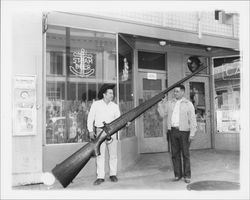 Two men with a giant wooden replica of a rifle, Petaluma, California, 1958