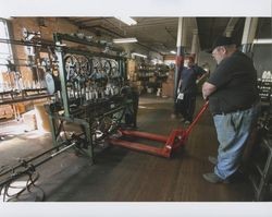 Russell Strickland stands by while "Big" Dennis Henderson inserts a pallet jack under a braider machine on the first floor of the Sunset Line & Twine Company building in Petaluma, California, Dec. 2006