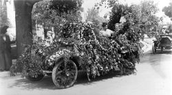 Car decorated with flowers and large doll sitting on the hood