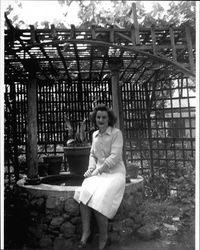 Ruth Agius seated on a stone well in the backyard of 210 West Street, Petaluma, California, about 1939