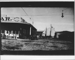 Sloop with sails extended, on the Petaluma River, passes B Street and the McNear Feed Company, Petaluma, California, 1897