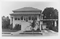 Unidentified woman standing on the steps of a two-story house with a large arbor over the side driveway, 1960s or 1970s