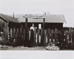 Dagny Juell standing under a sign reading "Troll Heimen,", about 1945