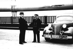 Lucien Benoit shaking hands with unidentified man while standing on the Golden Gate Bridge next to a car advertising Sonoma Rodeo at Millerick Ranch