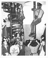 Fire Captain Jim Brian sliding down the firehouse pole surrounded by children, Petaluma, California, about 1963