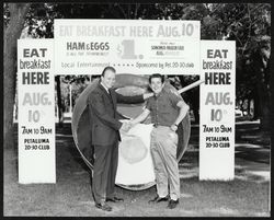 Dave Devoto and Jim Wallace stand in front of a giant frying pan to advertise the Petaluma 20-30 Club breakfast, 1961