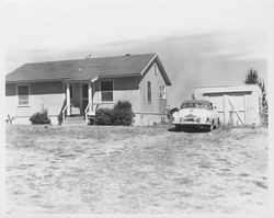 Unidentified single-story home with a late 1940s or early 1950s Dodge Business Coupe parked in the front of the garage, 1950s or 1960s