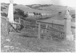 Fenced grave site at Bodega Cemetery with St. Teresa's Church and Potter school in background