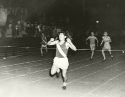 Analy High School Tigers track, 1960s--runner Phil Ito breaking the tape at a night time track meet