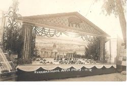 1912 Gravenstein Apple Show display of a decorated stage with classical style buildings in the background and apples and glasses in foreground