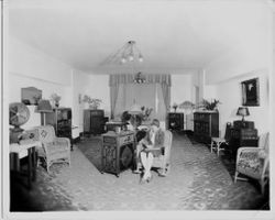 Interior of the Borba radio store with cabinet or console style radios and wicker chairs arranged around the room, 1920s