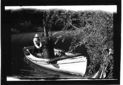 Small homemade steamboat with a man on board turning a crank handle on the Russian River, about 1900