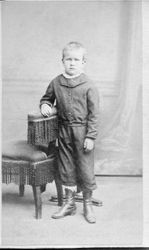 Unidentified young boy, about 6 years old standing next to a Victorian chair in a studio photo, about 1860s