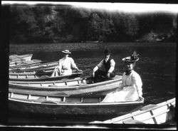 Three people in three separate boats--2 women and 1 man--among other empty boats apparently tied up to shore on the Russian River, about 1900