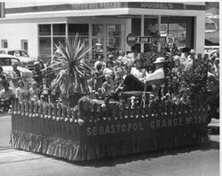 Harvey and Roberta Welter riding the Sebastopol Grange No. 306 float by the the McDonnell's Union Oil Dealer building in the, about 1956 Apple Blossom Parade in Sebastopol, California