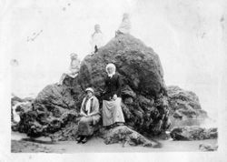 Three girls and two women sit or stand on a rock at Bodega Bay