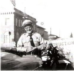 Sebastopol Police Officer Lemuel "Shorty" Plumley writing a traffic ticket on Main Street near the Bank of Sonoma County, about late 1940s or early 1950s