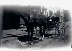 A. L. Strout in buggy with horse on a dirt street in front of wooden sidewalk and buildings, about 1903