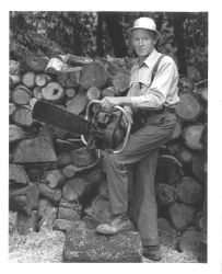 Ralph Sonoma Sturgeon standing in front of stack of logs holding a large chain saw