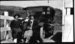 Two women on river ferry seated on front of a car with California license plates, about 1916