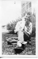 Unidentified teenage boy holding a cat and sitting in front of house