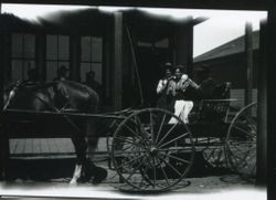 A. L. Strout in buggy drawn by a horse with three men standing on wooden walkway in front of building, about 1903