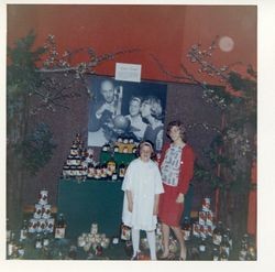 Donna Hallberg (Hallberg-Marovich and Kathie Hallberg , 1964 in front of Hallberg Apple Ranch display at the Gravenstein Apple Fair with enlarged photo of them with Gene Bologna, Sonoma County Sealer of Weights & Measures, weighing the large Hallberg apple